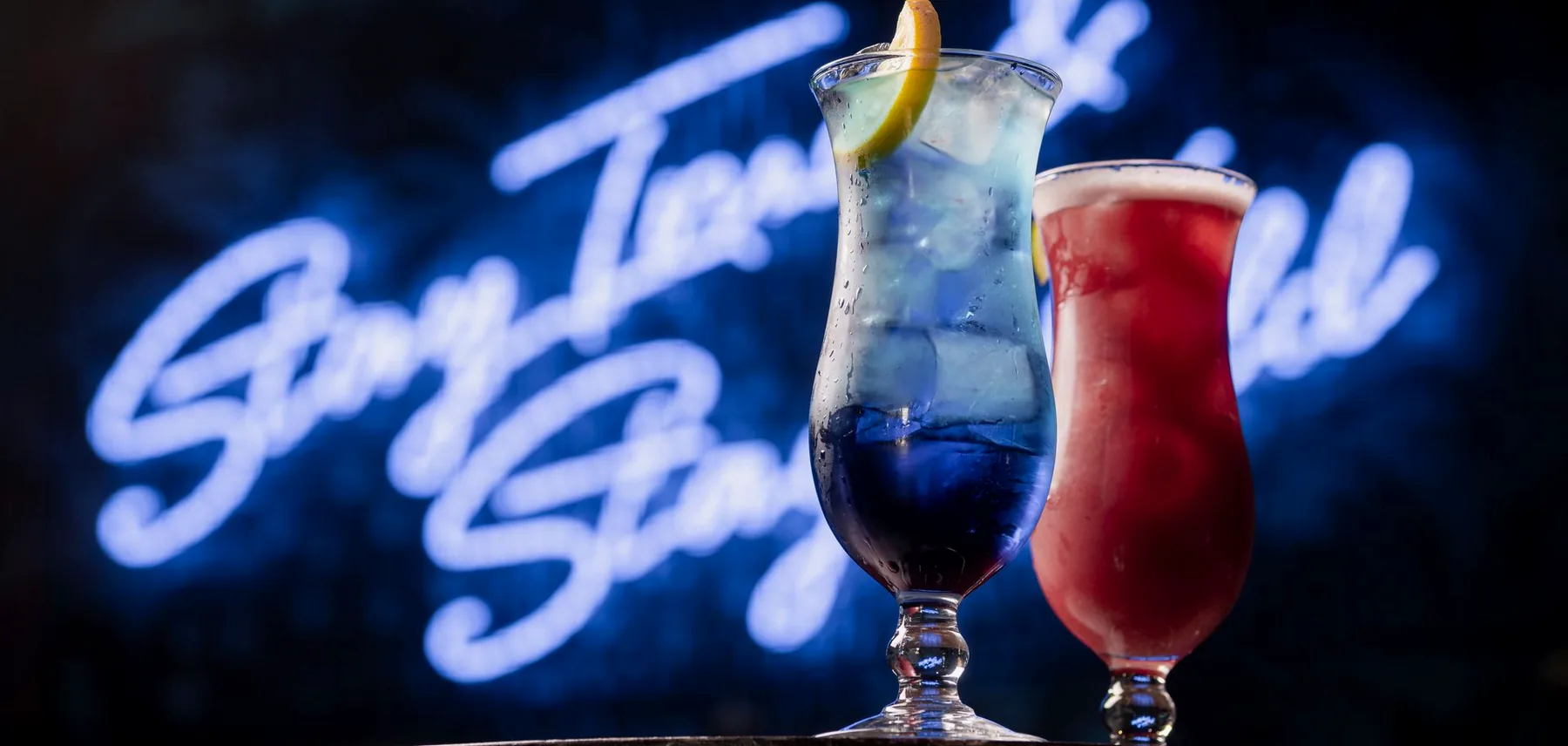Two cocktails on the bar in front of the Stay True Stay Wild neon