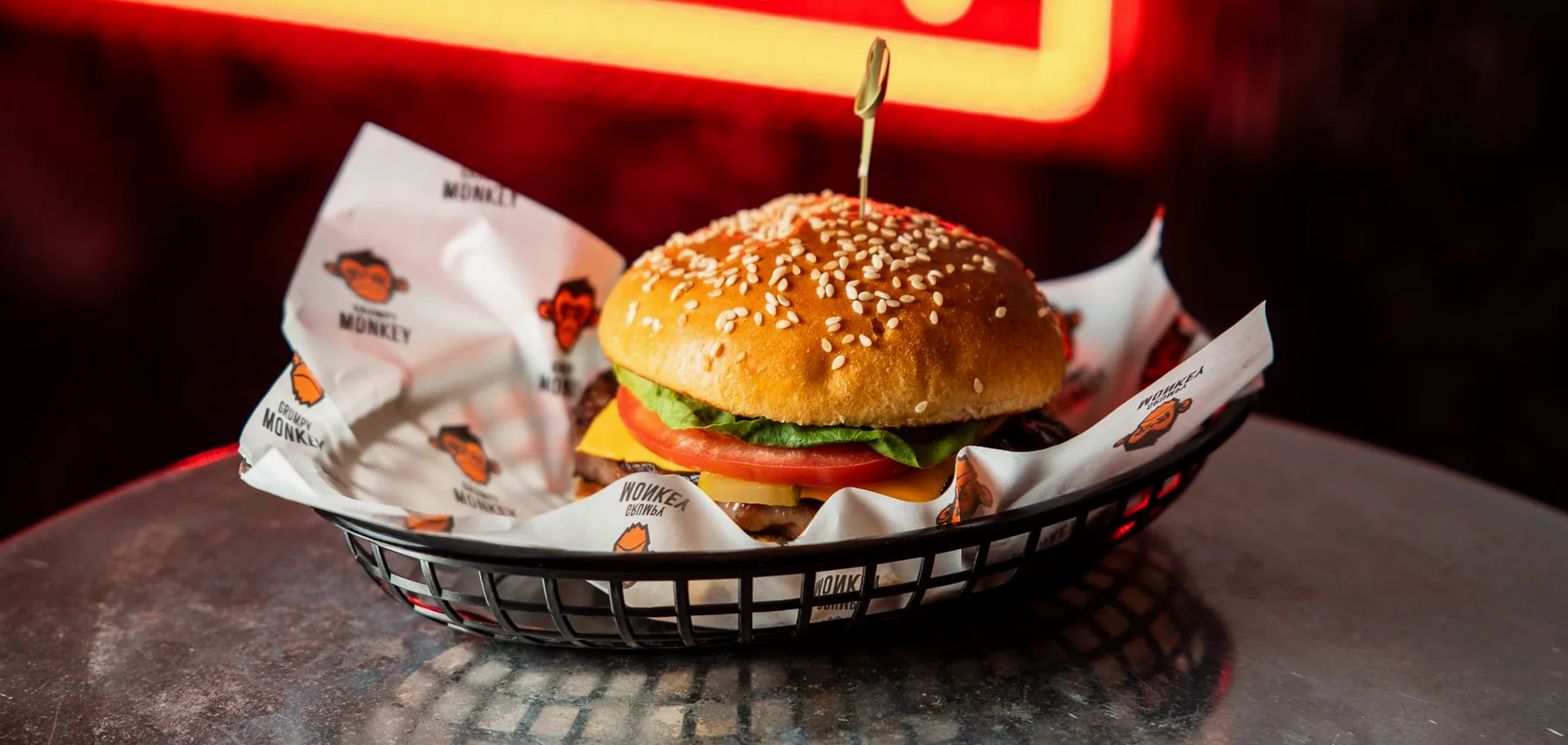 A Grumpy Monkey burger in a basket under the red neon sign